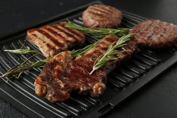 Delicious grilled beef meat with rosemary on black textured table, closeup