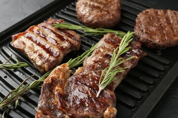 Delicious grilled beef meat with rosemary on black table, closeup
