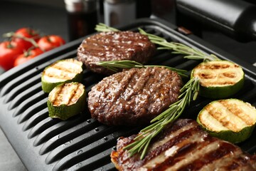 Electric grill with beef steaks, zucchini and rosemary on black table, closeup