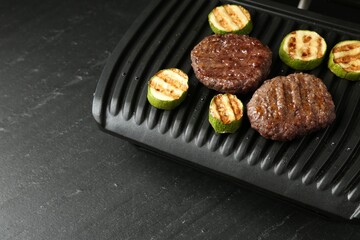 Electric grill with beef and zucchini on black table, closeup. Space for text