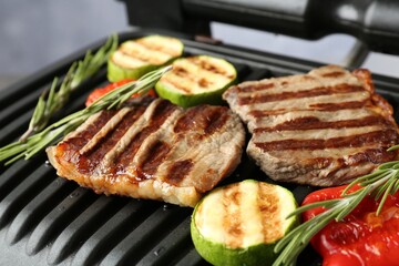 Electric grill with beef steaks, vegetables and rosemary on grey table, closeup