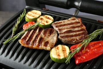 Electric grill with beef steaks, vegetables and rosemary on grey table, closeup
