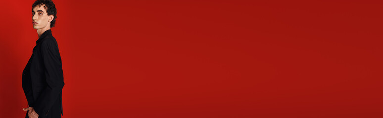 Stylish man in elegant attire poses confidently against a bold red backdrop