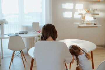 A mother lovingly braids her daughter's hair while they draw together, capturing a tender moment of family bonding and creative play. Perfect for parenting and lifestyle content