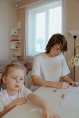 A mother lovingly braids her daughter's hair while they draw together, capturing a tender moment of family bonding and creative play. Perfect for parenting and lifestyle content