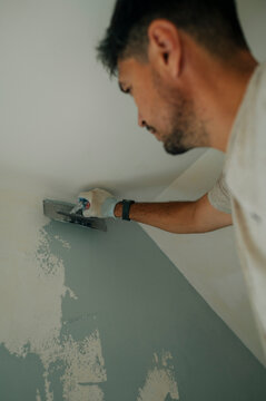 Worker plastering and repairing interior wall with trowel indoors