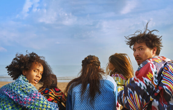 Diverse group in colorful robes at beach looking back with tense expressions