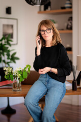 Blond haired confident woman sitting at desk at home and using her smartphone