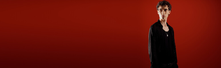 Handsome stylish man in elegant attire poses confidently against a vibrant red background