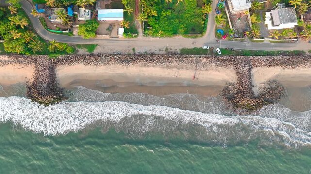 Aerial View of Rocky Seawall and Ocean Waves Crashing on Sandy Beach in Kerala, India