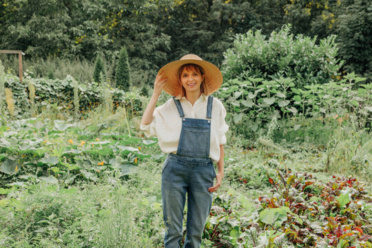 Woman in overalls with hat harvesting in vegetable garden outdoors