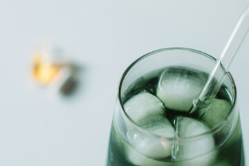 Tight crop of the chlorophyll iced glass with a glass straw, vitamins out of focus in the distance. Clean minimal look. Horizontal.