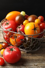 Different ripe tomatoes in basket on wooden table, closeup