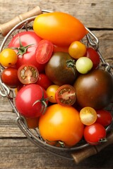 Different ripe tomatoes in basket on wooden table, top view