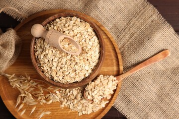 Oat flakes in bowl, scoop, spoon and florets on wooden table, flat lay