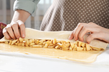Woman making delicious apple strudel at white table in kitchen, closeup