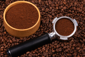 Holder with ground coffee on the background of roasted coffee beans with wooden cup. Coffee horn and coffee beans background texture.