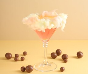 Tasty cocktail decorated with cotton candy and chocolate sweets on color background, closeup