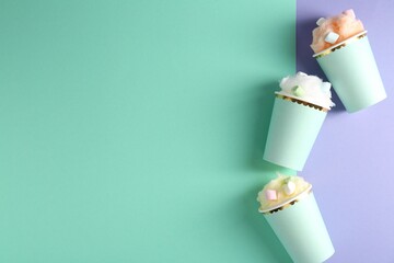 Cotton candy and marshmallows in paper cups on color background, flat lay. Space for text