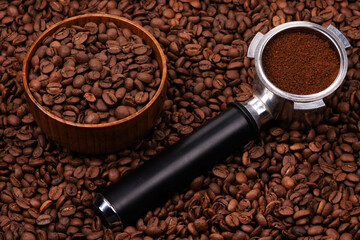 Holder with ground coffee on the background of roasted coffee beans with wooden cup. Coffee horn and coffee beans background texture.