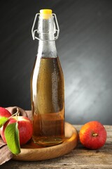 Delicious cider in glass bottle and apples on wooden table against dark gray background