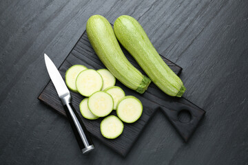 Fresh ripe zucchinis with knife on black textured table, top view. Whole and cut