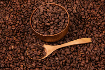 Wooden cup with coffee beans and wooden spoon on the background of roasted coffee beans. coffee beans background texture close up top view