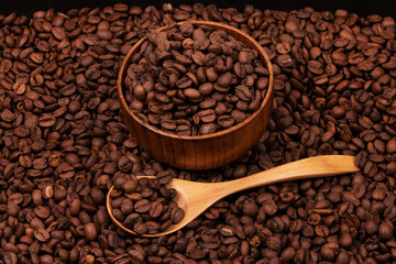Wooden cup with coffee beans and wooden spoon on the background of roasted coffee beans. coffee beans background texture close up top view
