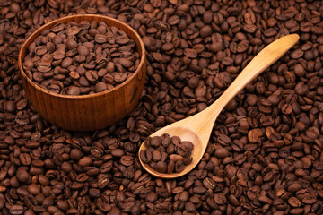 Wooden cup with coffee beans and wooden spoon on the background of roasted coffee beans. coffee beans background texture close up top view