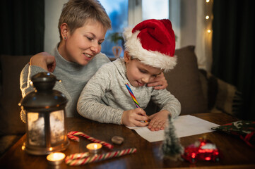 mother and son write letter to Santa Claus celebrate New Year and Christmas at home near decorated Christmas tree in cozy atmosphere 