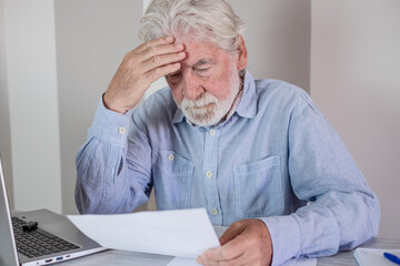 Elderly man looking stressed while reading documents at his desk, highlighting financial or administrative concerns.