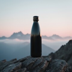 Matte black insulated water bottle placed on rocky mountain surface with misty peaks and soft pastel sunrise sky in background