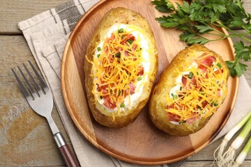 Tasty baked potatoes with sour cream, green onion, cheese and bacon served on wooden table, flat lay