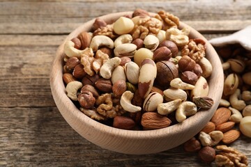 Mix of different nuts in bowl on wooden table, closeup