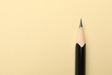 One sharp graphite pencil on beige background, top view. Space for text