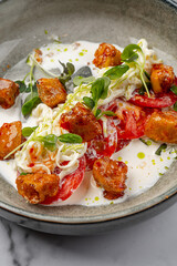 Gourmet salad with fresh tomatoes, soft cheese, crispy chicken bites, microgreens, and creamy dressing served in a modern ceramic bowl on marble background
