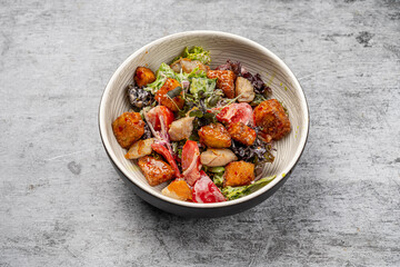 Fresh chicken salad with crispy fried pieces, lettuce, tomatoes, mixed greens, and dressing served in a ceramic bowl on gray background