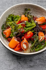 Fresh gourmet salad with smoked salmon rolls stuffed with cream cheese, cherry tomatoes, mixed greens, grapefruit segments, and microgreens served in a ceramic bowl on gray rustic background