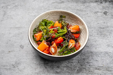 Fresh gourmet salad with smoked salmon rolls stuffed with cream cheese, cherry tomatoes, mixed greens, grapefruit segments, and microgreens served in a ceramic bowl on gray rustic background