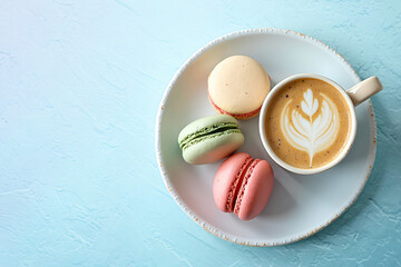 Multicolored French macarons on a plate, next to a cup of cappuccino with a pattern on a light blue vintage texture background. Top view.