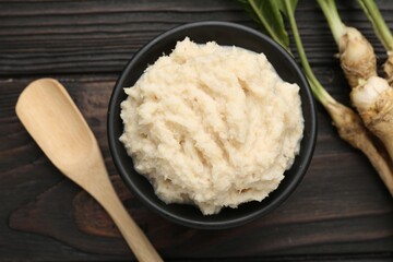 Tasty horseradish sauce and roots on black wooden table, flat lay