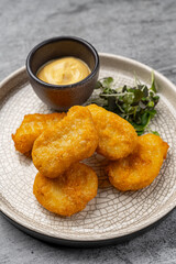Golden crispy chicken nuggets served with creamy dipping sauce and fresh microgreens on a white ceramic plate with cracked texture on gray background