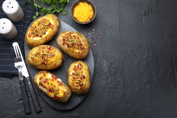 Tasty stuffed baked potatoes served on black textured table, flat lay. Space for text