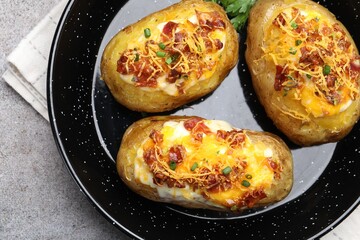 Tasty stuffed baked potatoes in baking dish on grey table, top view