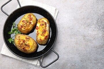 Tasty stuffed baked potatoes in baking dish on grey table, top view. Space for text