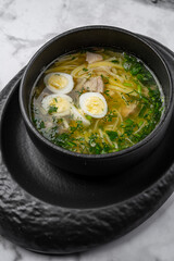 Traditional chicken noodle soup with boiled egg slices, fresh dill, and vegetables served in a black ceramic bowl on marble table