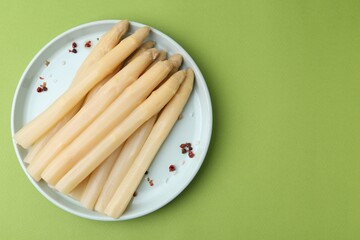Pickled asparagus spears with spices on green table, top view. Space for text
