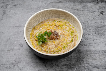 Creamy mushroom risotto with parmesan cheese, fresh herbs and olive oil drizzle served in a ceramic bowl on gray stone background