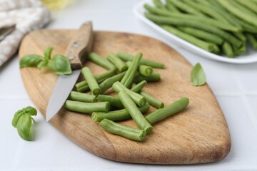 Cut green bean pods and knife on white table, closeup