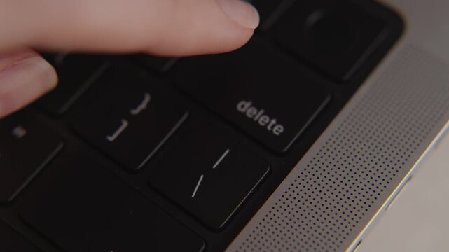 Finger pressing delete key on laptop keyboard, concept of erasing, removing files, data protection, online security, business decision and digital control